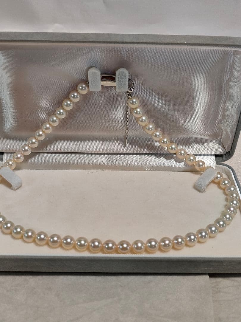 Akoya pearl necklace with white 7mm pearls and silver beans-shaped slide clasp on a plain background