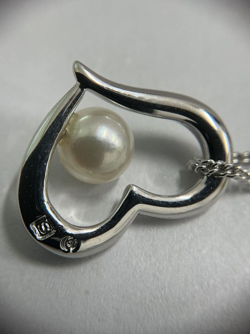 Silver color necklace featuring a heart motif decorated with a pearl and a hook clasp