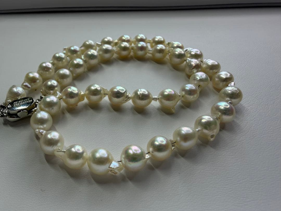 Akoya pearl necklace with 7.5mm white pearls and silver clasp laid flat on white background