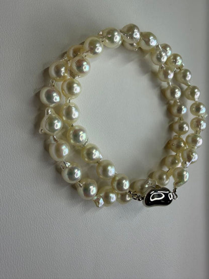 Akoya pearl necklace with 7.5mm white pearls and silver clasp laid flat on white background