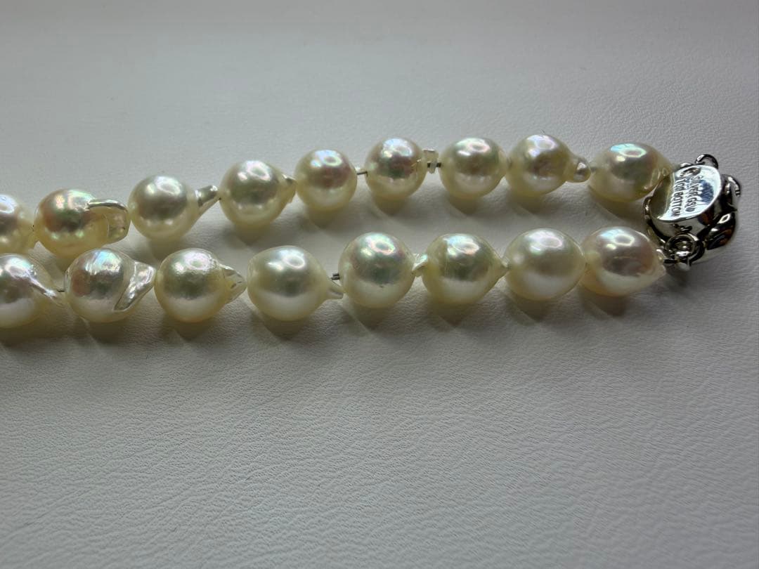 Akoya pearl necklace with 7.5mm white pearls and silver clasp laid flat on white background