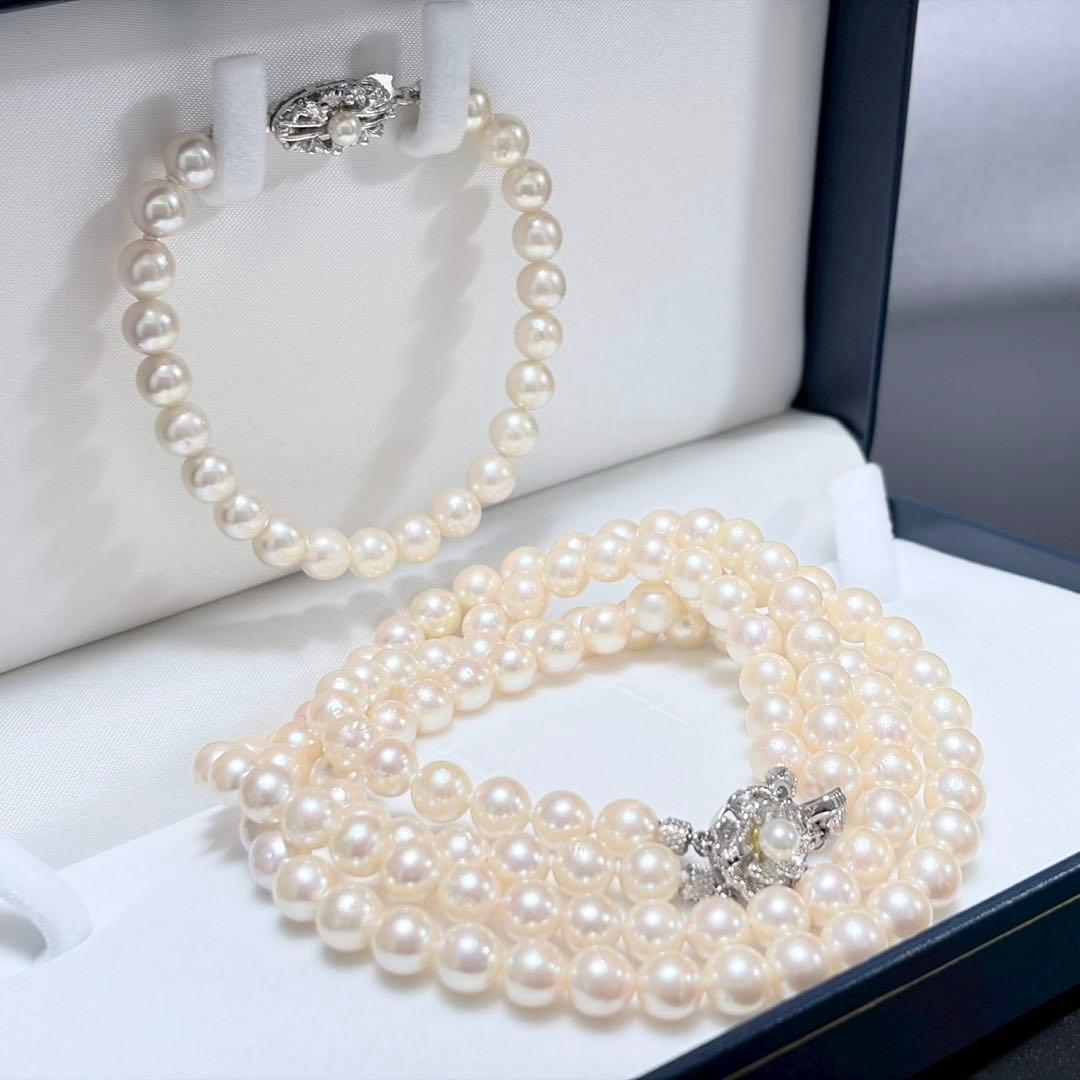 Akoya pearl double strand necklace and matching bracelet with silver clasp laid out on white background