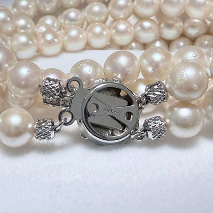 Akoya pearl double strand necklace and matching bracelet with silver clasp laid out on white background
