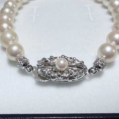 Akoya pearl double strand necklace and matching bracelet with silver clasp laid out on white background