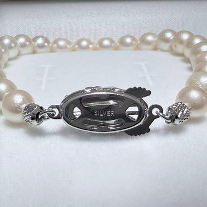 Akoya pearl double strand necklace and matching bracelet with silver clasp laid out on white background