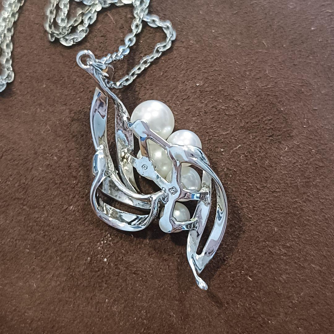 Mikimoto pearl necklace with grape-colored pearls and slightly discolored chain displayed on white background