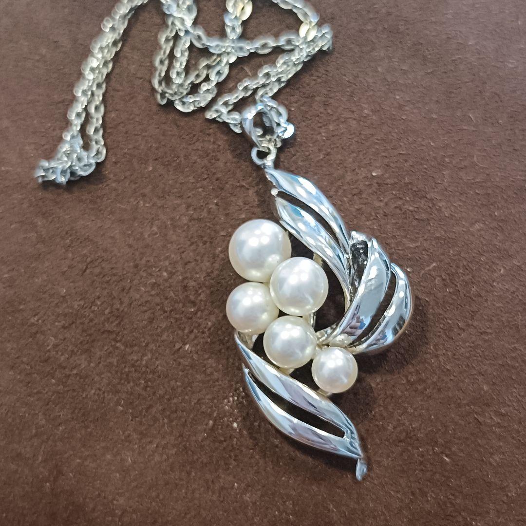 Mikimoto pearl necklace with grape-colored pearls and slightly discolored chain displayed on white background