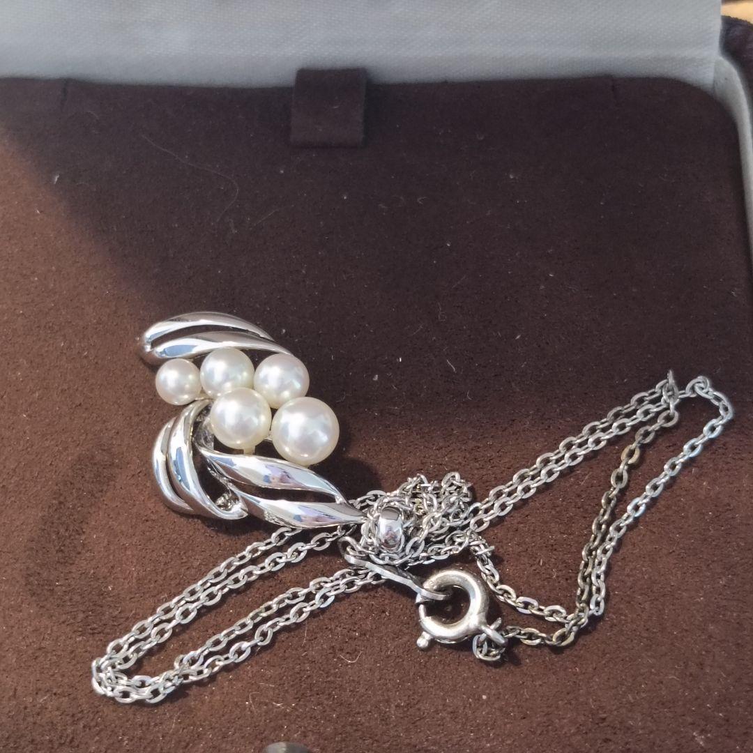 Mikimoto pearl necklace with grape-colored pearls and slightly discolored chain displayed on white background