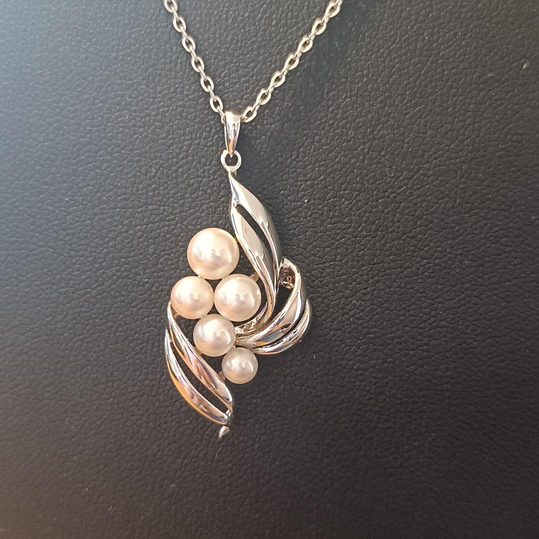 Mikimoto pearl necklace with grape-colored pearls and slightly discolored chain displayed on white background