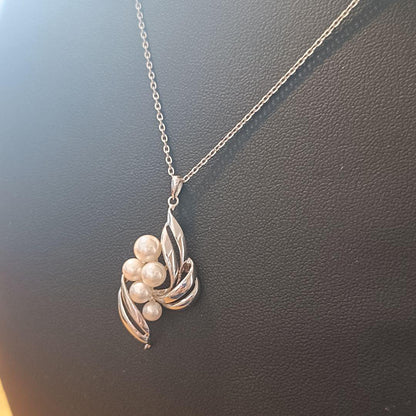 Mikimoto pearl necklace with grape-colored pearls and slightly discolored chain displayed on white background
