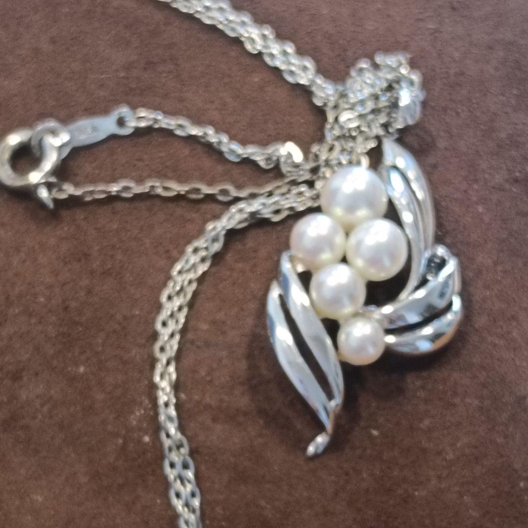 Mikimoto pearl necklace with grape-colored pearls and slightly discolored chain displayed on white background