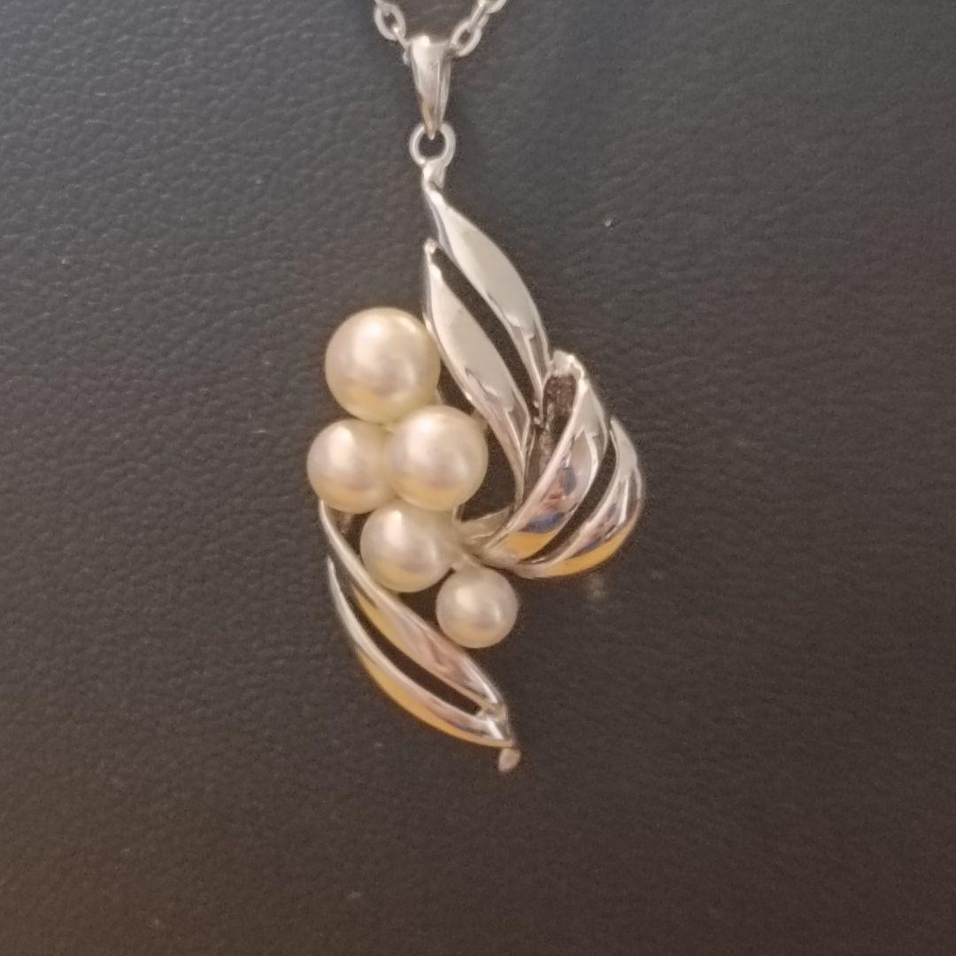 Mikimoto pearl necklace with grape-colored pearls and slightly discolored chain displayed on white background