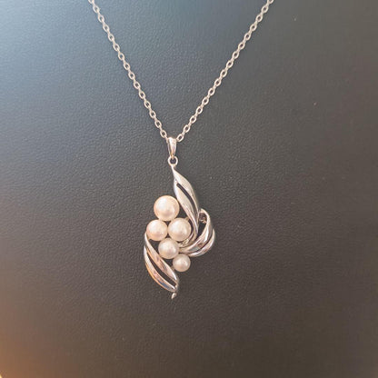 Mikimoto pearl necklace with grape-colored pearls and slightly discolored chain displayed on white background