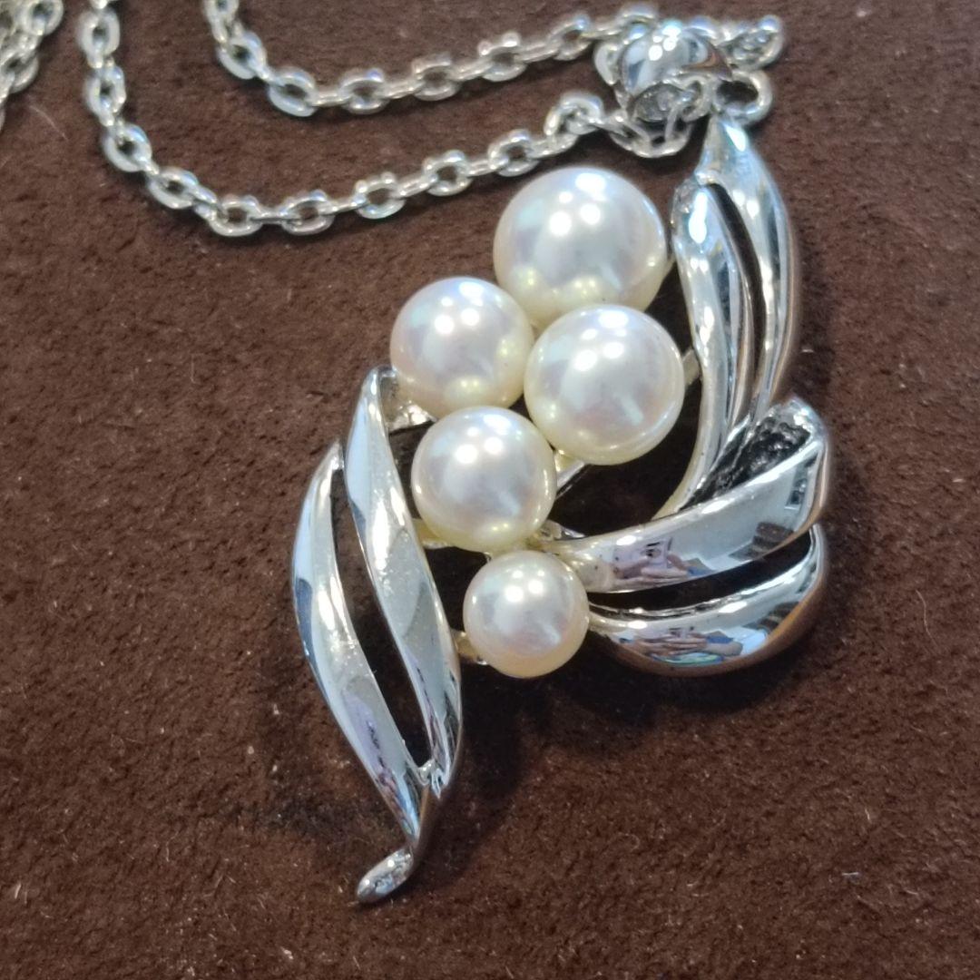Mikimoto pearl necklace with grape-colored pearls and slightly discolored chain displayed on white background