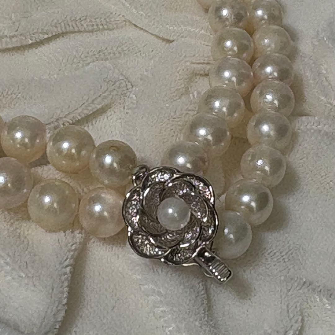 Akoya pearl necklace and matching earrings with silver engraved flower clasp on a white background
