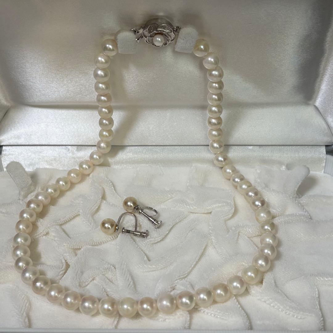 Akoya pearl necklace and matching earrings with silver engraved flower clasp on a white background