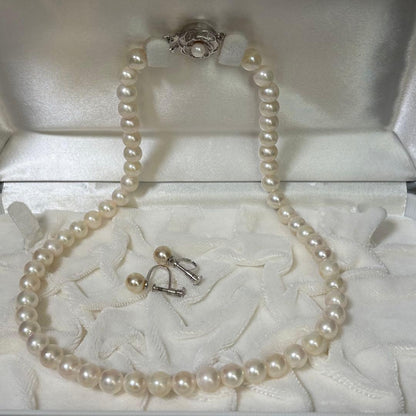 Akoya pearl necklace and matching earrings with silver engraved flower clasp on a white background