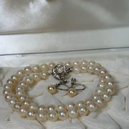 Akoya pearl necklace and matching earrings with silver engraved flower clasp on a white background