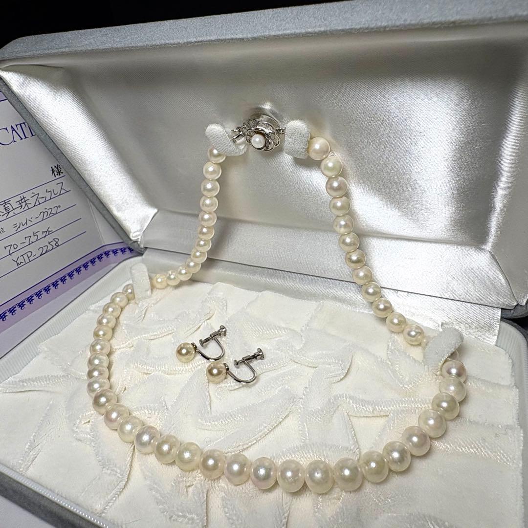 Akoya pearl necklace and matching earrings with silver engraved flower clasp on a white background