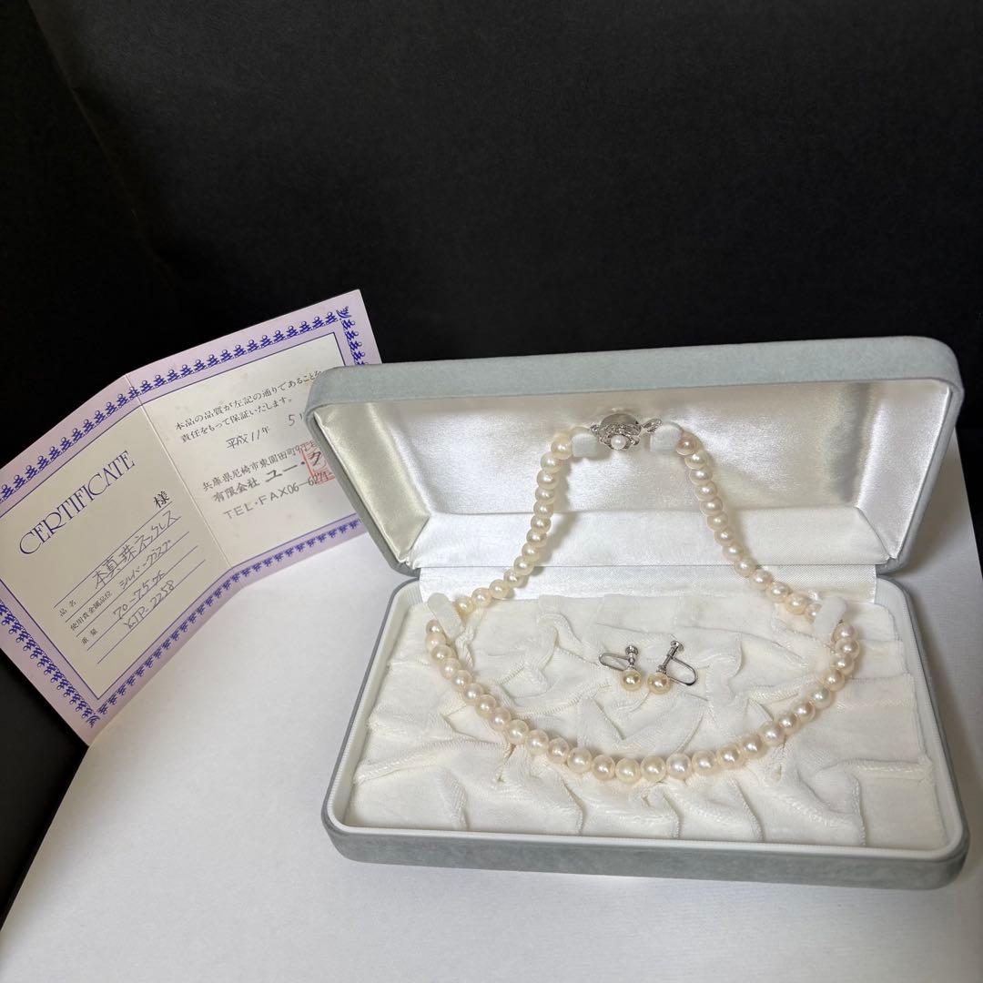 Akoya pearl necklace and matching earrings with silver engraved flower clasp on a white background