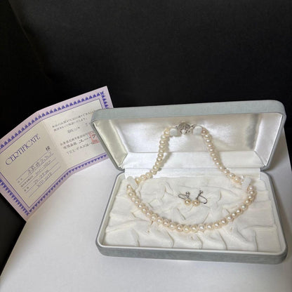 Akoya pearl necklace and matching earrings with silver engraved flower clasp on a white background