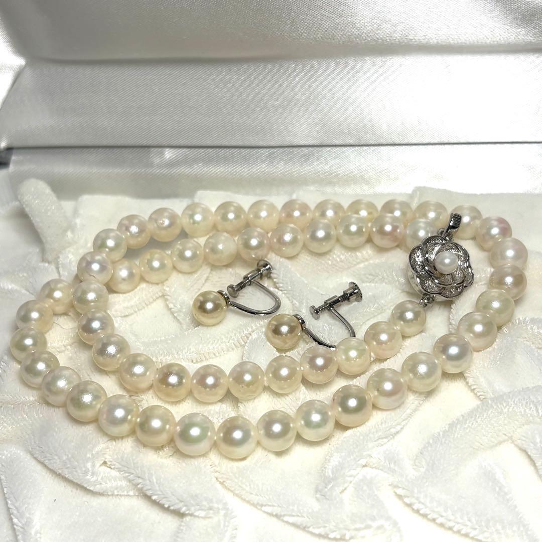 Akoya pearl necklace and matching earrings with silver engraved flower clasp on a white background