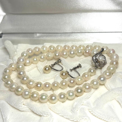 Akoya pearl necklace and matching earrings with silver engraved flower clasp on a white background