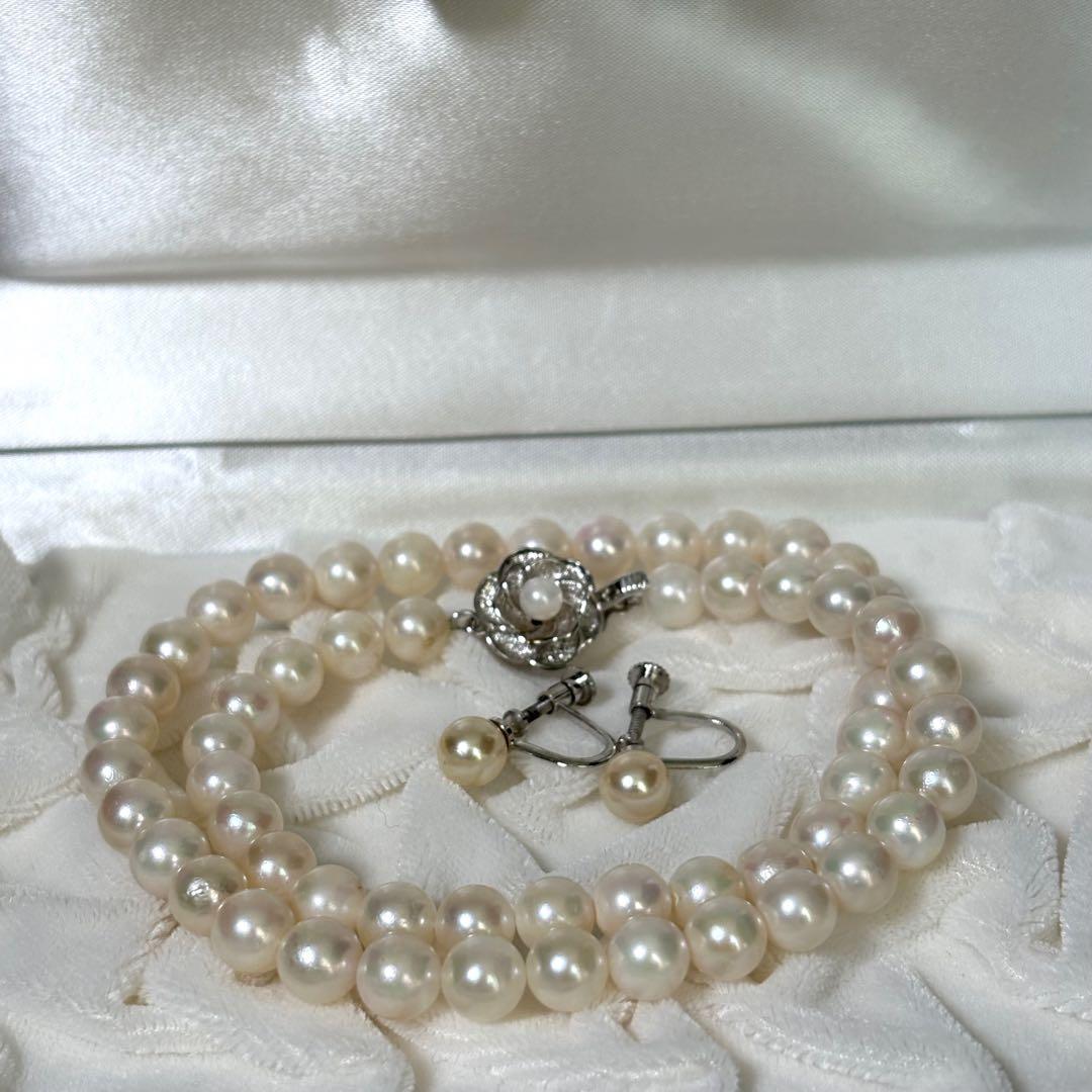 Akoya pearl necklace and matching earrings with silver engraved flower clasp on a white background