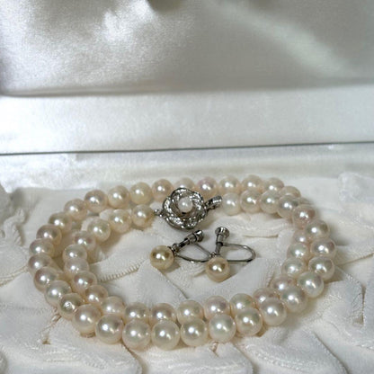 Akoya pearl necklace and matching earrings with silver engraved flower clasp on a white background