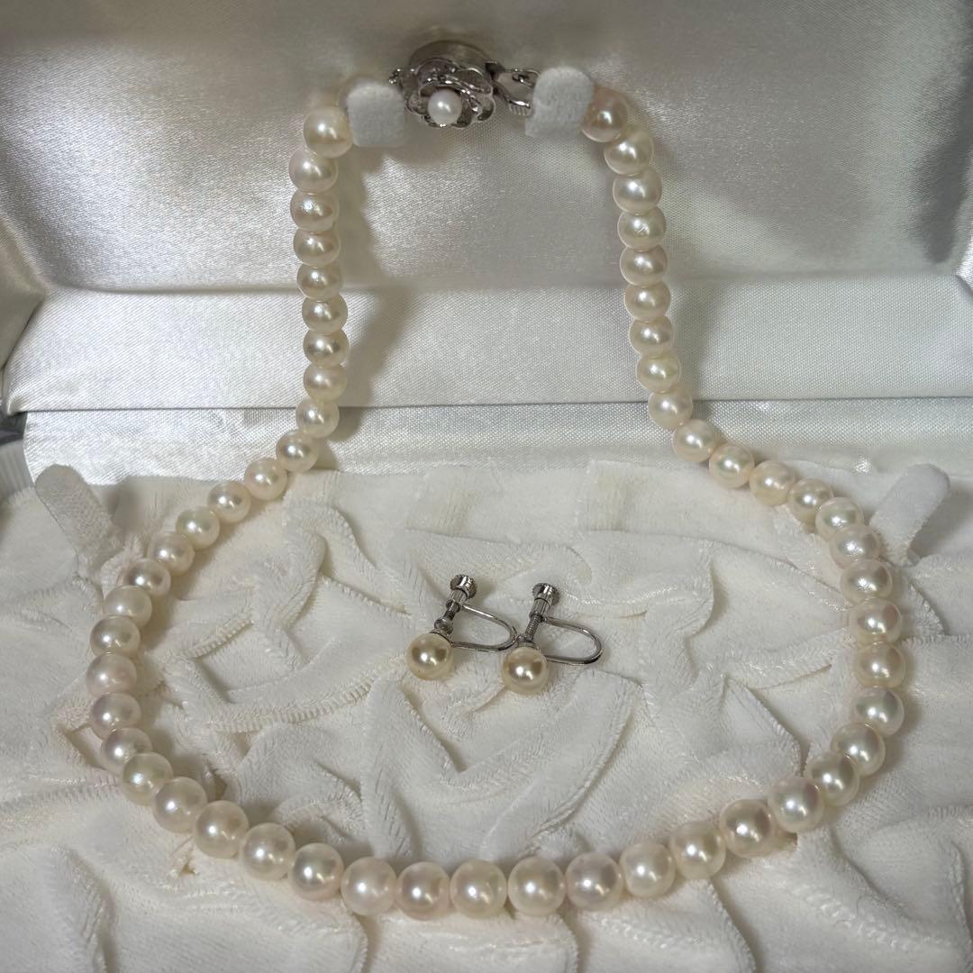 Akoya pearl necklace and matching earrings with silver engraved flower clasp on a white background