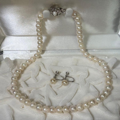 Akoya pearl necklace and matching earrings with silver engraved flower clasp on a white background