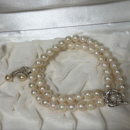 Akoya pearl necklace and matching earrings with silver engraved flower clasp on a white background