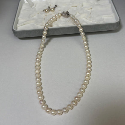 Akoya pearl necklace and matching earrings with silver engraved flower clasp on a white background