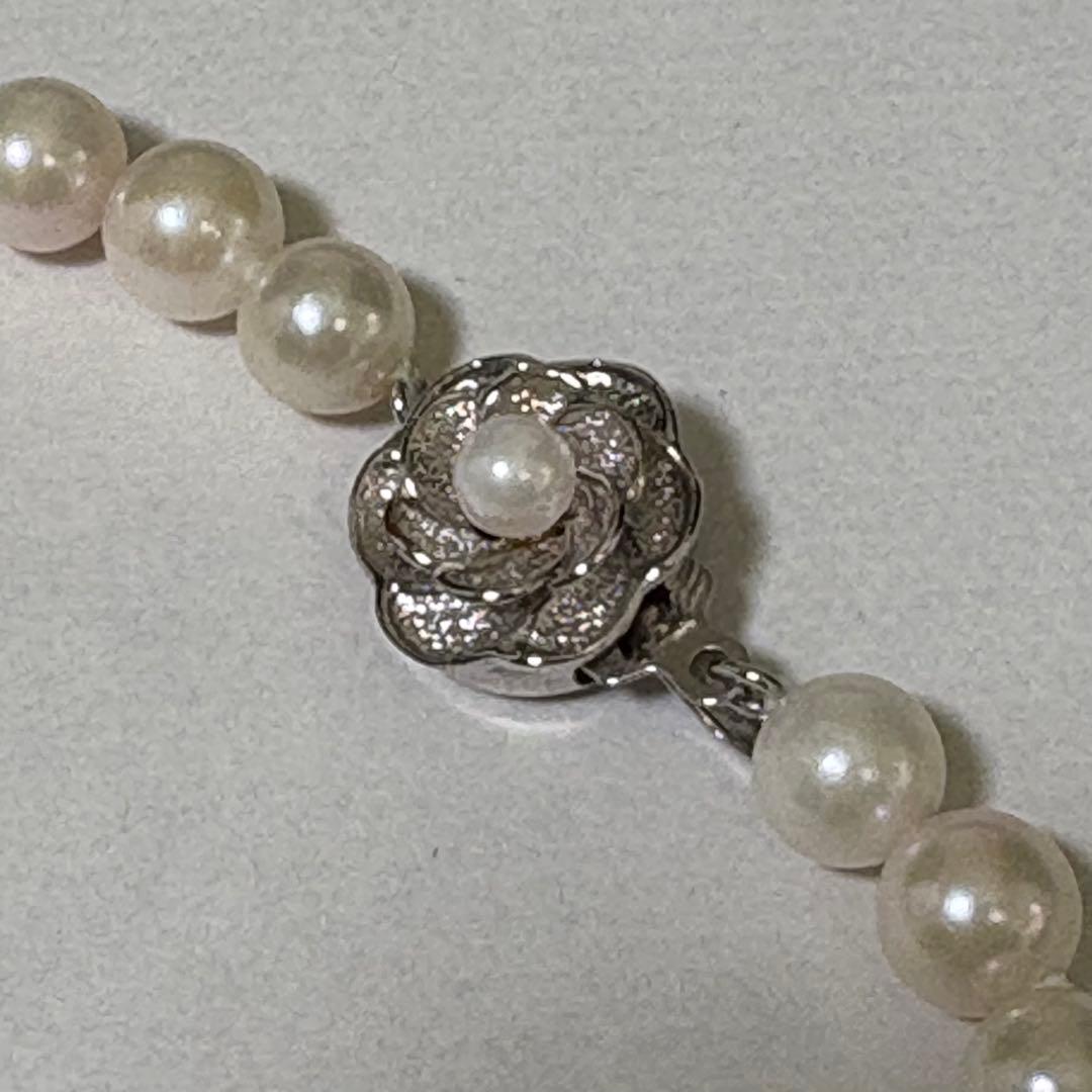 Akoya pearl necklace and matching earrings with silver engraved flower clasp on a white background