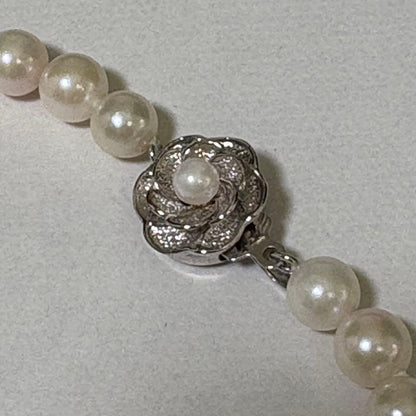 Akoya pearl necklace and matching earrings with silver engraved flower clasp on a white background