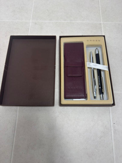 Two CROSS ballpoint pens in silver and black alongside a leather-like pen case