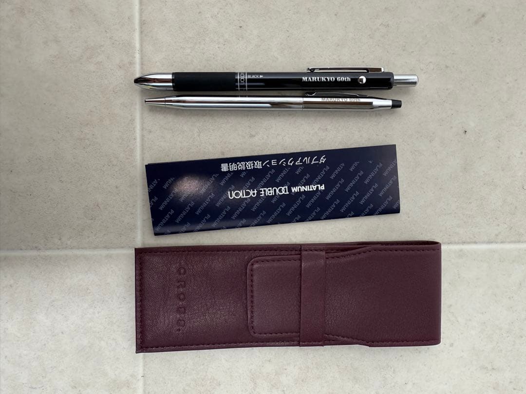 Two CROSS ballpoint pens in silver and black alongside a leather-like pen case