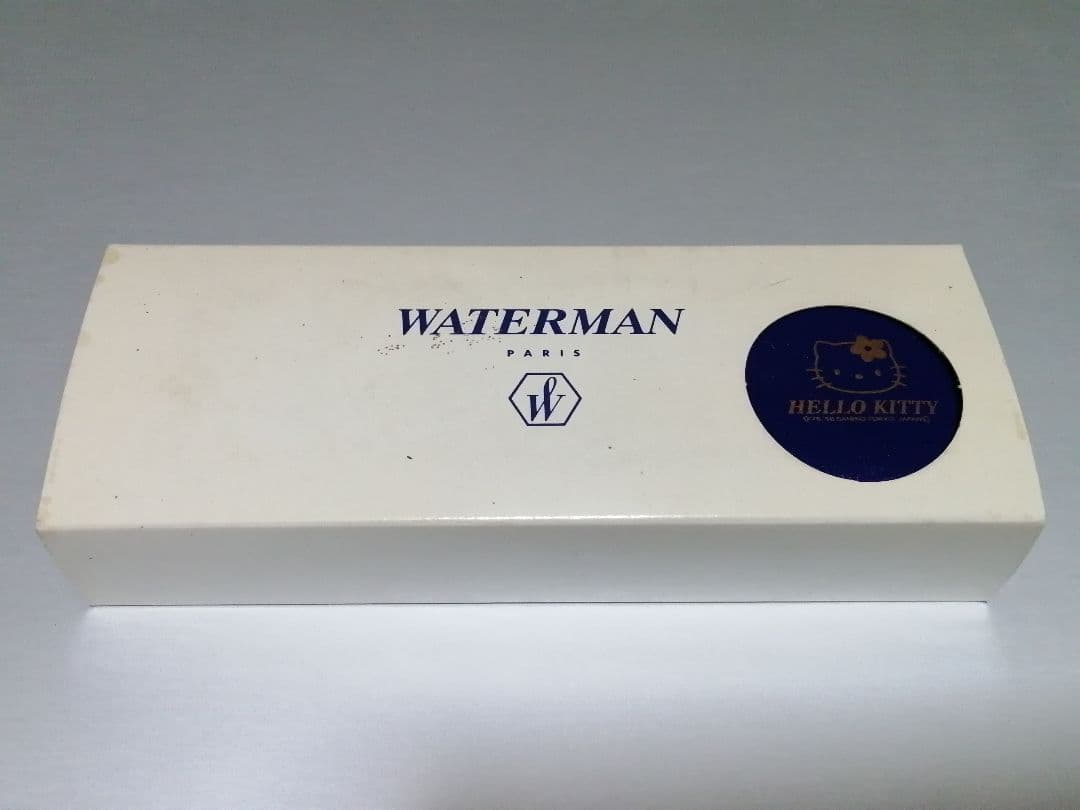 Hello Kitty Waterman ballpoint pen with extra ink refill, external box, and vintage storage case showing yellowing