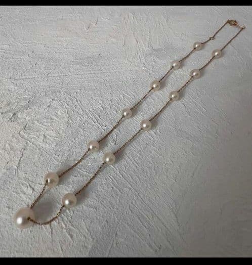 Beautiful K18 gold chain Akoya pearl necklace with 13 round pearls sized 6.5 to 9.5 mm on a white background
