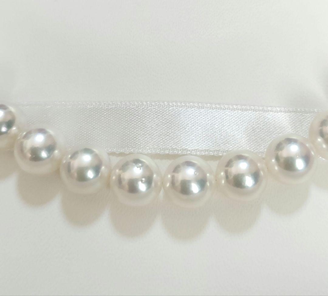Akoya pearl large round necklace with white pearls and pink-green light interference on a white background