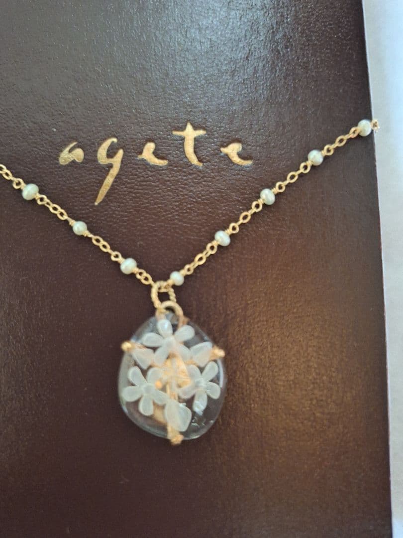 agete flower motif necklace with gold flower pendant and metal chain displayed with dedicated box