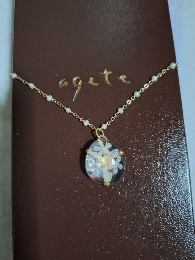 agete flower motif necklace with gold flower pendant and metal chain displayed with dedicated box