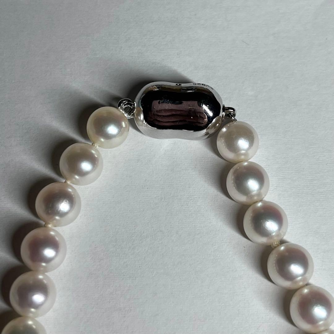 Close-up of Akoya pearl necklace with white pearls showing pink and green interference colors and silver clasp