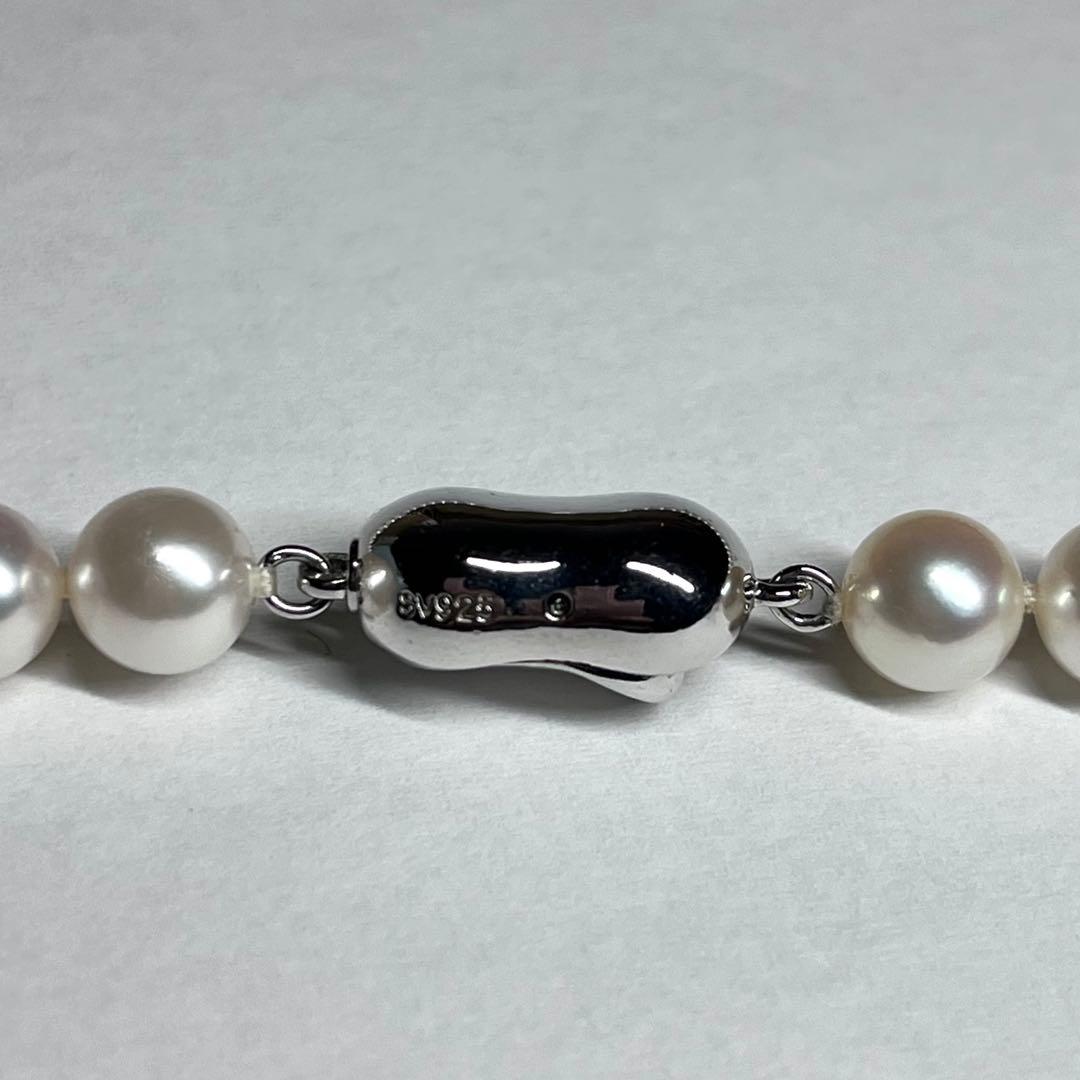 Close-up of Akoya pearl necklace with white pearls showing pink and green interference colors and silver clasp