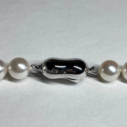 Close-up of Akoya pearl necklace with white pearls showing pink and green interference colors and silver clasp