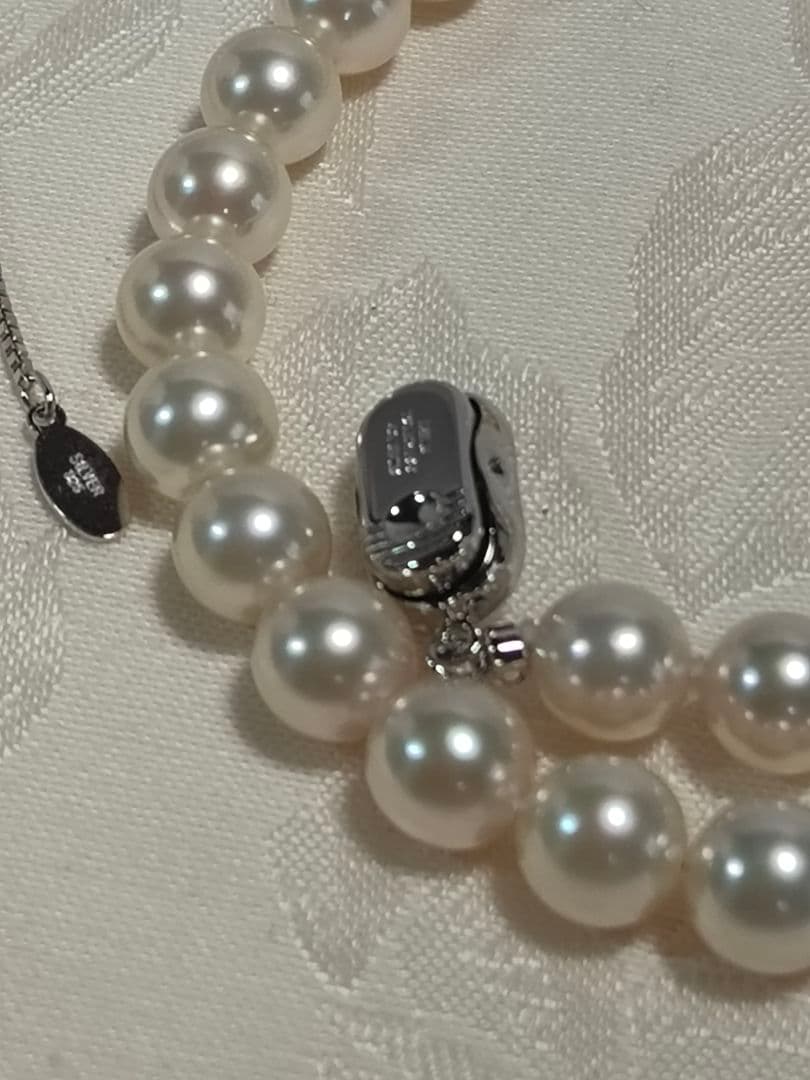 Akoya pearl necklace with white 7mm pearls and silver beans-shaped slide clasp on a plain background