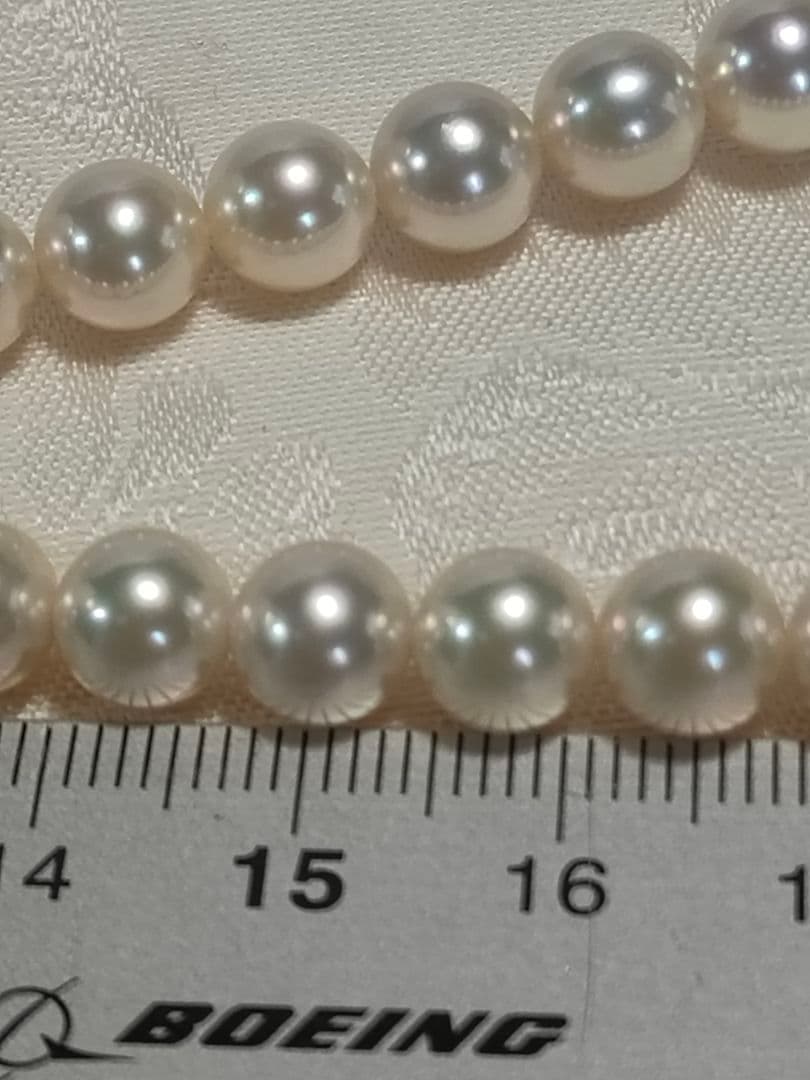 Akoya pearl necklace with white 7mm pearls and silver beans-shaped slide clasp on a plain background