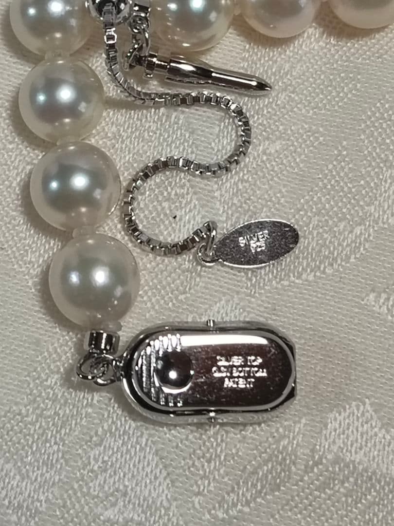 Akoya pearl necklace with white 7mm pearls and silver beans-shaped slide clasp on a plain background