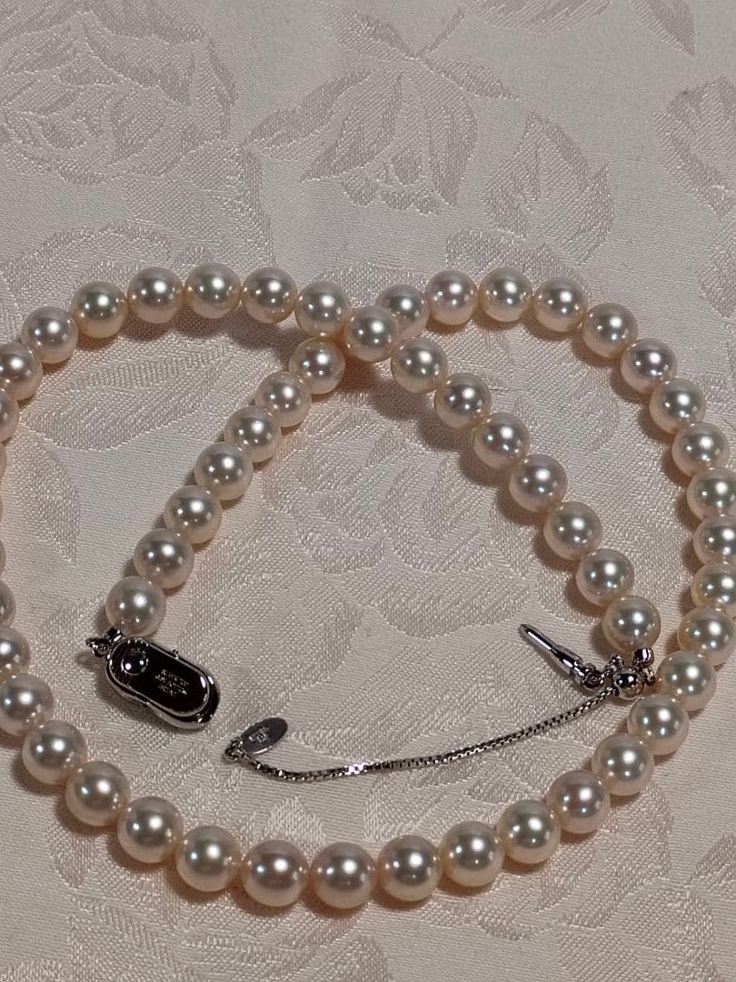 Akoya pearl necklace with white 7mm pearls and silver beans-shaped slide clasp on a plain background