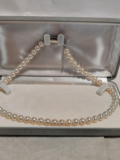 Akoya pearl necklace with white 7mm pearls and silver beans-shaped slide clasp on a plain background